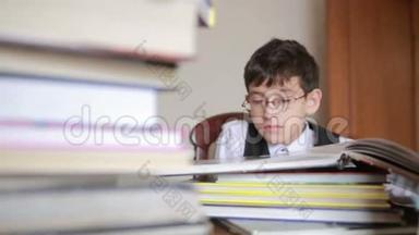 男孩坐在<strong>一</strong>张桌子旁，桌上放着<strong>一叠书</strong>。 孩子读<strong>书</strong>。 戴眼镜的男孩